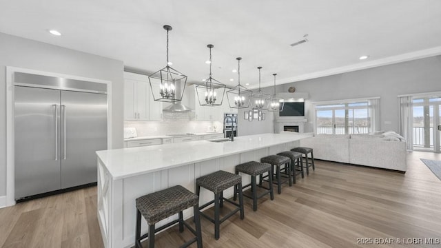 5450 Christopher Dr Unit 243, Osage Beach, MO 65065 - kitchen with stainless steel built in refrigerator, white cabinetry, wall chimney range hood, light wood-style flooring, and tasteful backsplash