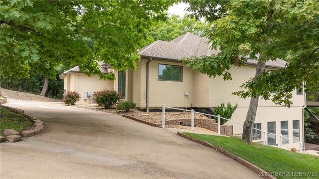 135 Greensboro Ct, Four Seasons, MO 65049 - view of property exterior with driveway, stucco siding, and roof with shingles