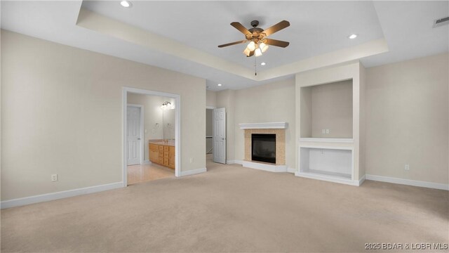 135 Greensboro Ct, Four Seasons, MO 65049 - unfurnished living room featuring a tray ceiling, light colored carpet, ceiling fan, recessed lighting, and a glass covered fireplace