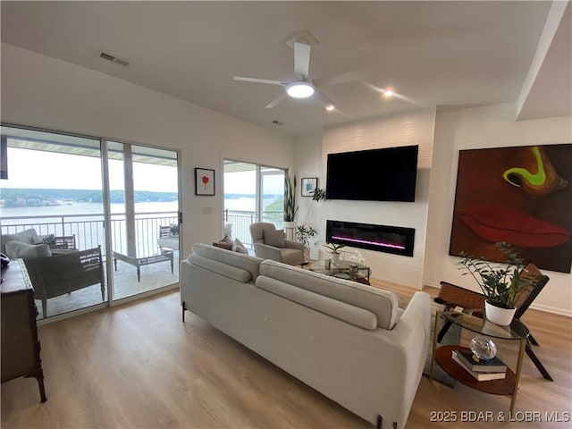 42 Palisades Lakeview Dr Unit 4B, Lake Ozark, MO 65049 - living room with wood finished floors, a glass covered fireplace, a ceiling fan, and a water view