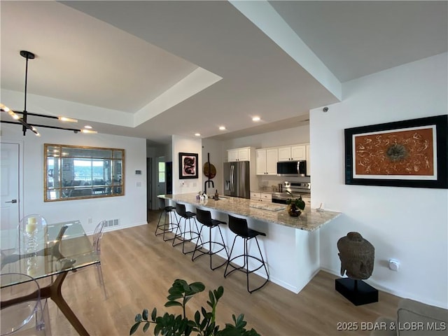 42 Palisades Lakeview Dr Unit 4B, Lake Ozark, MO 65049 - kitchen featuring appliances with stainless steel finishes, light stone counters, white cabinets, a breakfast bar, and light wood finished floors