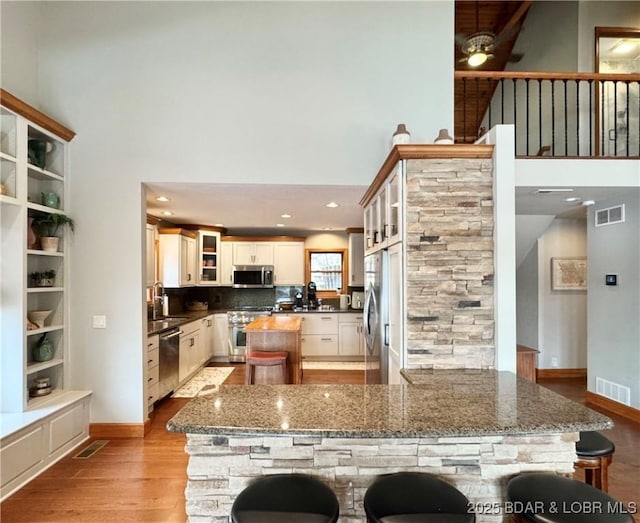 158 Oak Manor Cir, Sunrise Beach, MO 65079 - kitchen with appliances with stainless steel finishes, a high ceiling, light wood-type flooring, a kitchen island, and glass insert cabinets