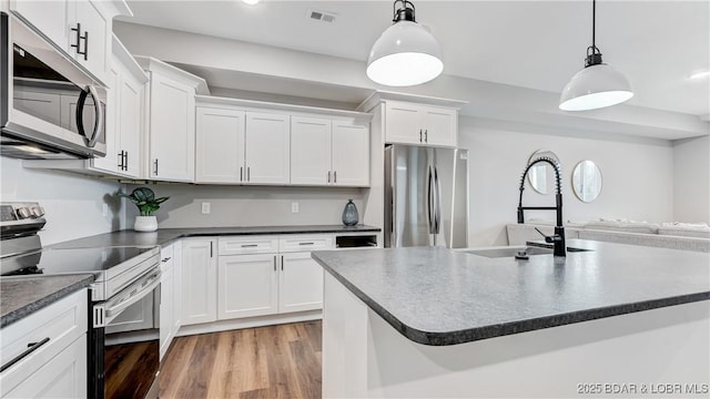 104 Sierra Bay Dr Unit 1B, Camdenton, MO 65020 - kitchen featuring stainless steel appliances, dark countertops, white cabinets, hanging light fixtures, and light wood-style floors