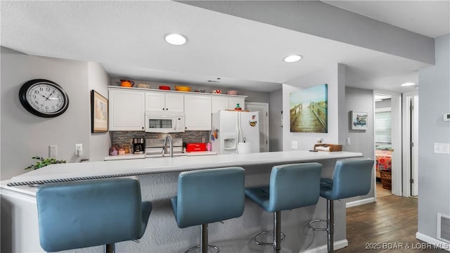 1201 W Harbour Towne Dr Unit 1201, Lake Ozark, MO 65049 - kitchen with white appliances, a kitchen breakfast bar, decorative backsplash, dark wood finished floors, and white cabinets