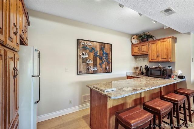 1078 Cornett Branch Rd, Lake Ozark, MO 65049 - kitchen featuring black microwave, freestanding refrigerator, light stone counters, a peninsula, and a breakfast bar