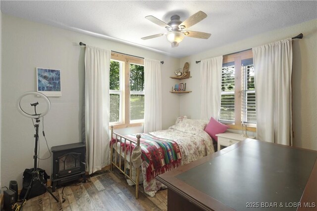 5109 Aqua Dr, Osage Beach, MO 65065 - bedroom with wood finished floors, a wood stove, ceiling fan, and a textured ceiling