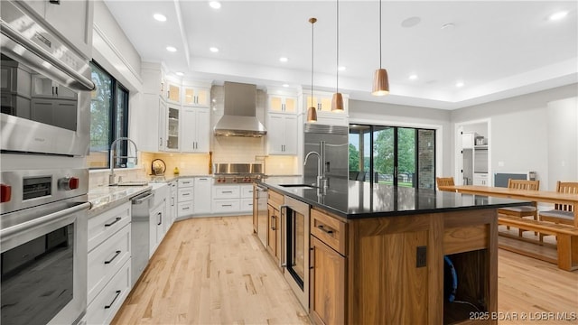 1254 Darwin Dr, Osage Beach, MO 65065 - kitchen featuring wall chimney range hood, wine cooler, stainless steel appliances, light wood finished floors, and decorative backsplash