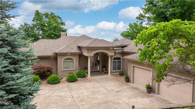 1453 Grand View Dr, Porto Cima, MO 65079 - view of front of property featuring stucco siding, a garage, roof with shingles, driveway, and a chimney