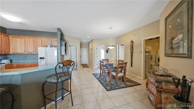 1230 Lands End Pkwy Unit 304, Osage Beach, MO 65065 - kitchen with white fridge with ice dispenser, washer and dryer, light tile patterned flooring, a kitchen bar, and light countertops
