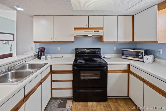 278 Lone Oak Pt Unit 18, Sunrise Beach, MO 65079 - kitchen featuring black range with electric cooktop, stainless steel microwave, under cabinet range hood, white cabinets, and wood finished floors