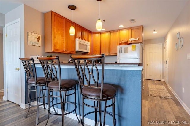1481 Ledges Dr Unit C24, Osage Beach, MO 65065 - kitchen featuring white appliances, wood finished floors, a peninsula, a kitchen bar, and decorative light fixtures