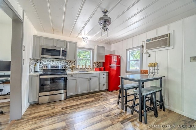 54 White Rock Ln, Sunrise Beach, MO 65079 - kitchen with stainless steel appliances, gray cabinetry, a wall unit AC, backsplash, and light wood-type flooring