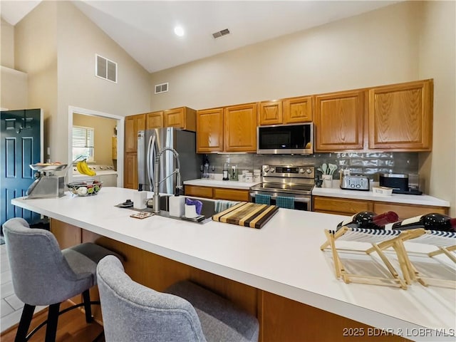 110 Golf View Dr, Camdenton, MO 65020 - kitchen featuring appliances with stainless steel finishes, high vaulted ceiling, washing machine and dryer, a breakfast bar, and tasteful backsplash