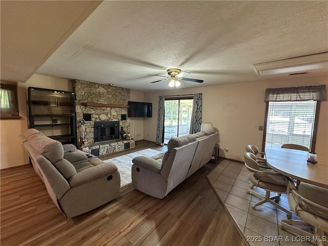 30024 Hawaii Rd, Gravois Mills, MO 65037 - living room featuring wood finished floors, a textured ceiling, a stone fireplace, and ceiling fan