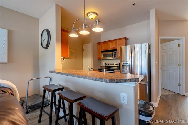 275 Flynn Rd Unit 105, Lake Ozark, MO 65049 - kitchen featuring stainless steel appliances, wood finished floors, brown cabinets, a breakfast bar area, and a peninsula