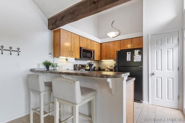 392 Hopetown Dr, Osage Beach, MO 65065 - kitchen with stainless steel microwave, freestanding refrigerator, light tile patterned floors, a peninsula, and dark countertops