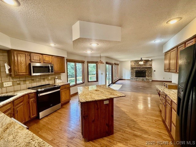 170 Twin Oaks Dr, Lake Ozark, MO 65049 - kitchen with stainless steel appliances, a textured ceiling, open floor plan, a kitchen island, and brown cabinetry