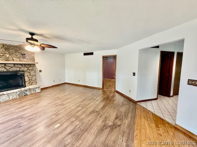 170 Twin Oaks Dr, Lake Ozark, MO 65049 - unfurnished living room featuring ceiling fan, wood finished floors, a stone fireplace, and a textured ceiling