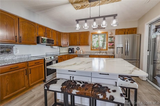 35 Port Bagnell W, Eldon, MO 65026 - kitchen with stainless steel appliances, light wood-type flooring, brown cabinetry, and hanging light fixtures