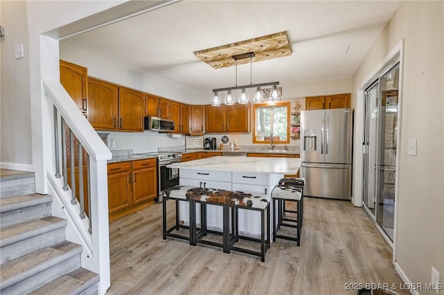 35 Port Bagnell W, Eldon, MO 65026 - kitchen with appliances with stainless steel finishes, brown cabinetry, light wood-type flooring, a kitchen breakfast bar, and pendant lighting