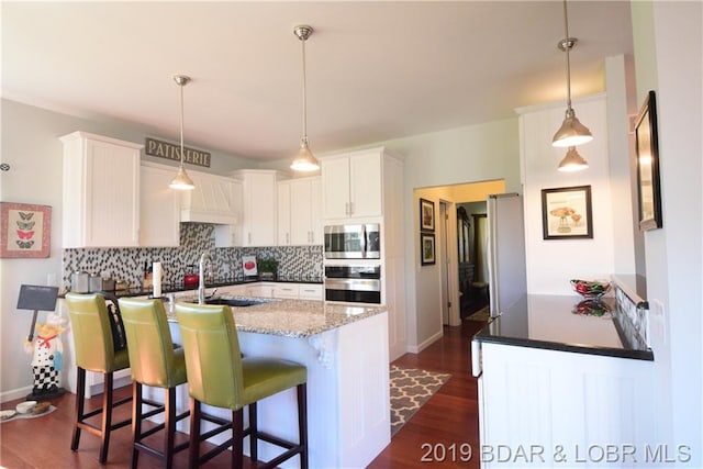 kitchen with hanging light fixtures, dark hardwood / wood-style floors, stone countertops, appliances with stainless steel finishes, and tasteful backsplash