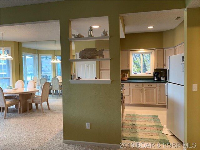 kitchen featuring light brown cabinetry, white refrigerator, light colored carpet, and pendant lighting