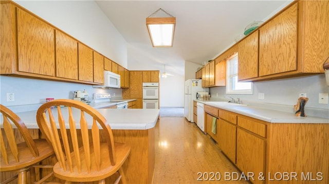 kitchen with a kitchen breakfast bar, white appliances, light wood-type flooring, and sink