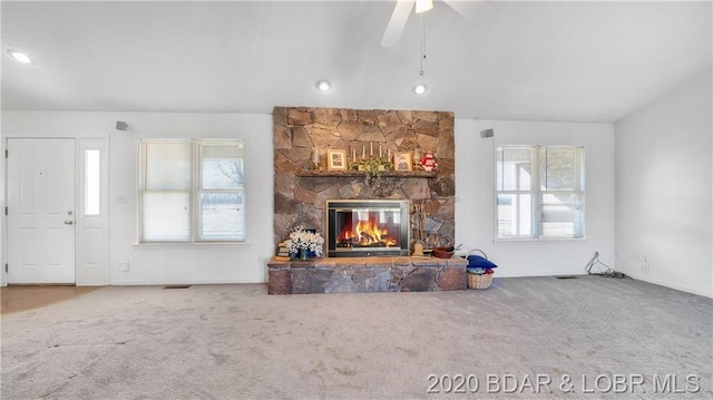 carpeted living room with a stone fireplace, ceiling fan, and a wealth of natural light