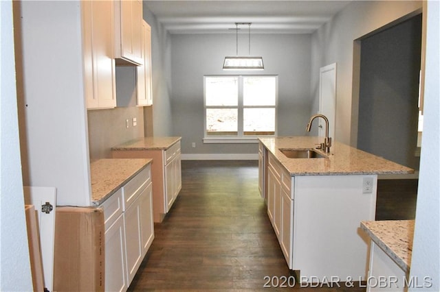 kitchen featuring an island with sink, pendant lighting, sink, light stone counters, and dark hardwood / wood-style flooring