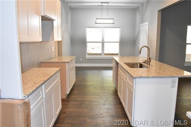 kitchen featuring dark hardwood / wood-style floors, sink, light stone counters, hanging light fixtures, and a center island with sink