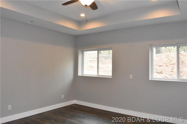 unfurnished room featuring dark hardwood / wood-style flooring, ceiling fan, and a tray ceiling