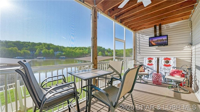 sunroom with ceiling fan and a water view