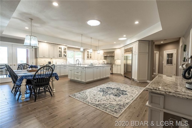 kitchen featuring sink, built in fridge, wall chimney exhaust hood, decorative light fixtures, and a center island