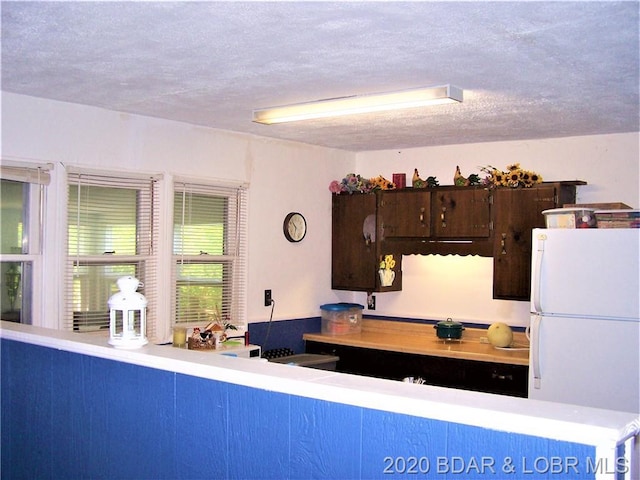 kitchen featuring a textured ceiling, white fridge, and dark brown cabinetry