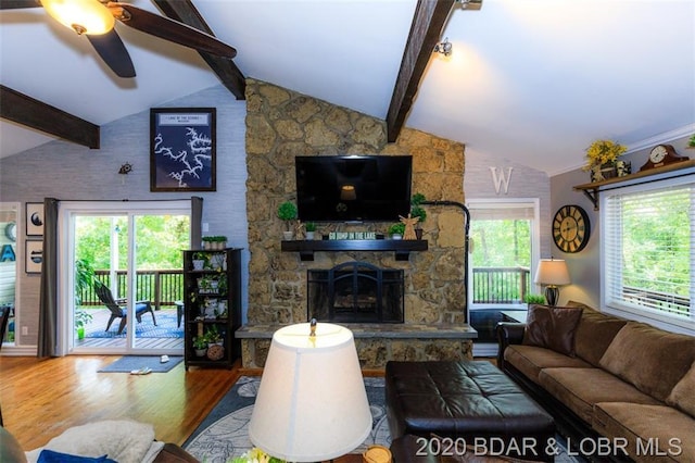 living room featuring ceiling fan, a stone fireplace, vaulted ceiling with beams, and dark wood-type flooring