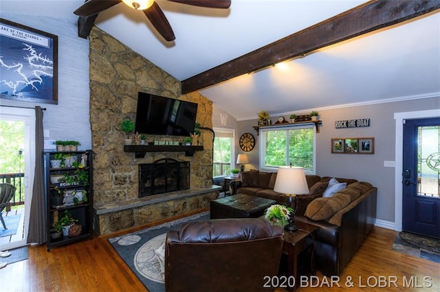 living room with ceiling fan, lofted ceiling with beams, dark wood-type flooring, and a stone fireplace