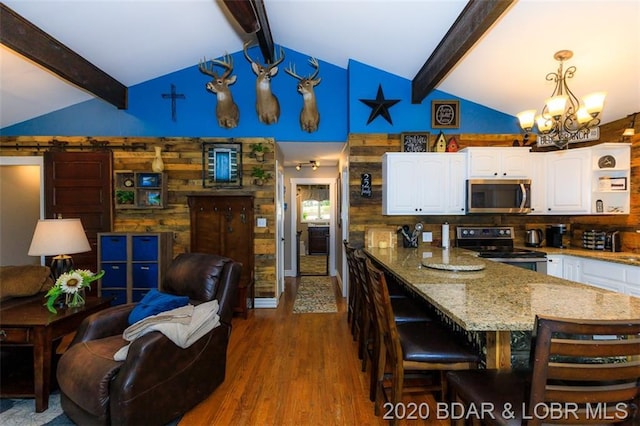 kitchen with a notable chandelier, range with electric stovetop, beam ceiling, white cabinets, and a breakfast bar area