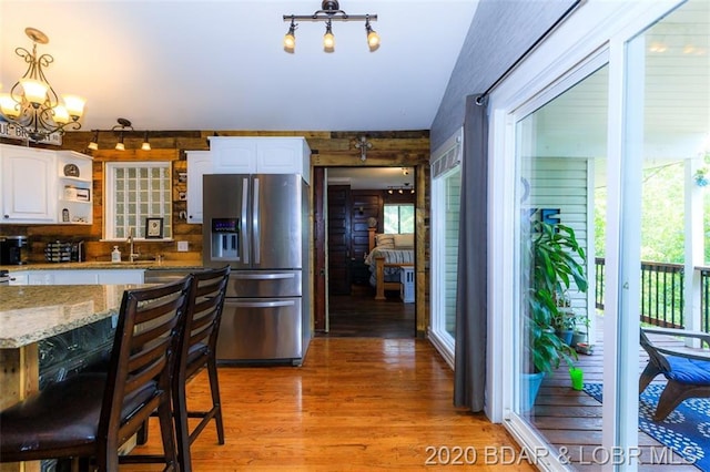 kitchen featuring a notable chandelier, hardwood / wood-style flooring, a kitchen bar, stainless steel fridge with ice dispenser, and white cabinets