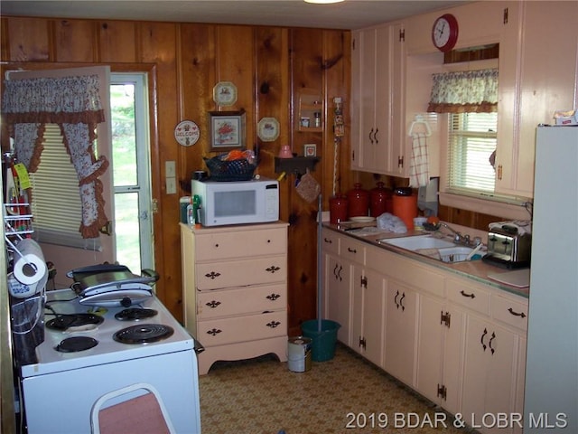 kitchen with wood walls, light colored carpet, white cabinetry, white appliances, and sink