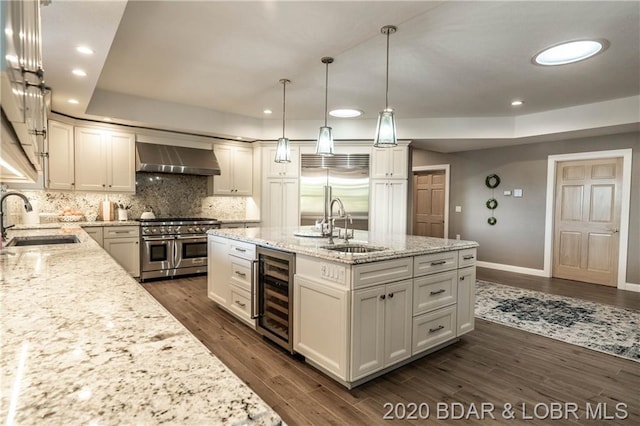 kitchen with high quality appliances, wall chimney range hood, wine cooler, white cabinetry, and sink