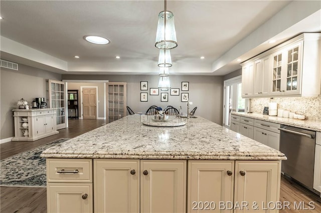 kitchen with an island with sink, light stone counters, dark hardwood / wood-style flooring, stainless steel dishwasher, and decorative light fixtures