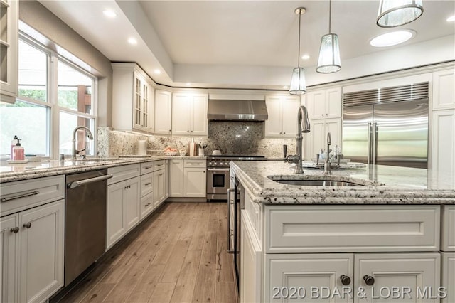 kitchen with pendant lighting, light hardwood / wood-style flooring, high end appliances, wall chimney range hood, and white cabinetry