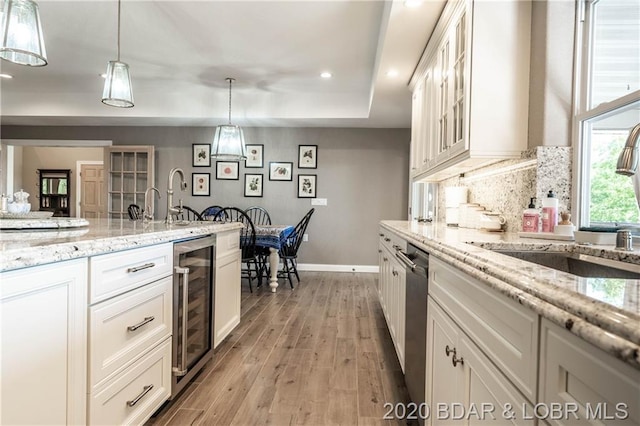 kitchen featuring beverage cooler, hanging light fixtures, white cabinetry, and light hardwood / wood-style floors