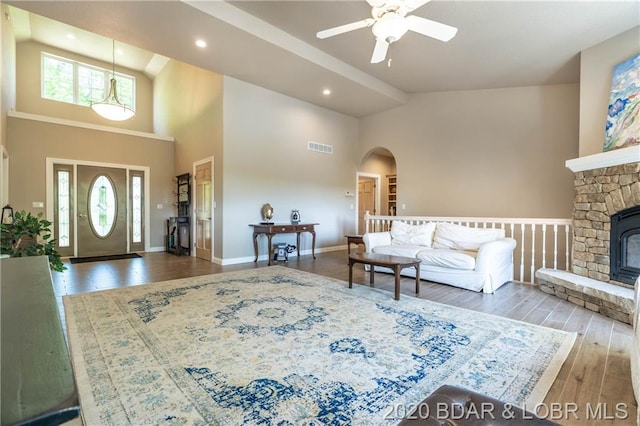 foyer with a towering ceiling, ceiling fan, a stone fireplace, and wood-type flooring