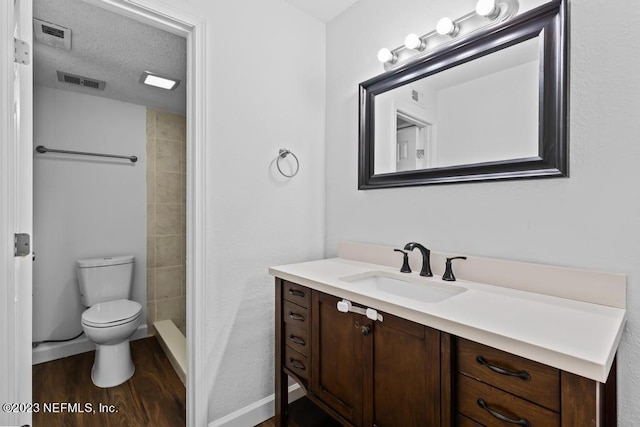 bathroom featuring a textured ceiling, hardwood / wood-style flooring, tiled shower, vanity, and toilet