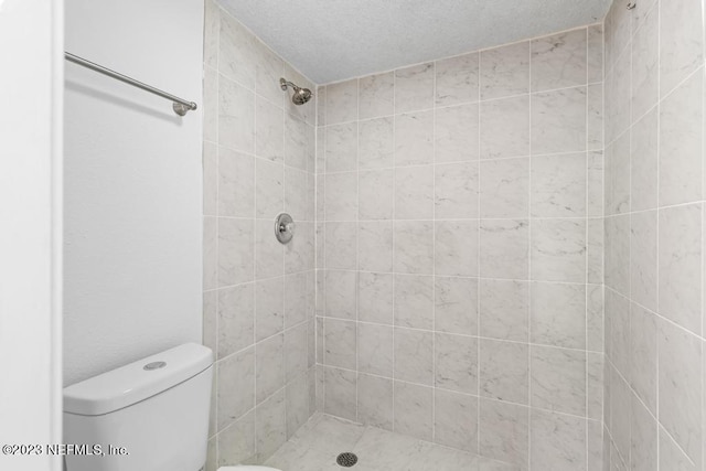 bathroom with a tile shower, a textured ceiling, and toilet