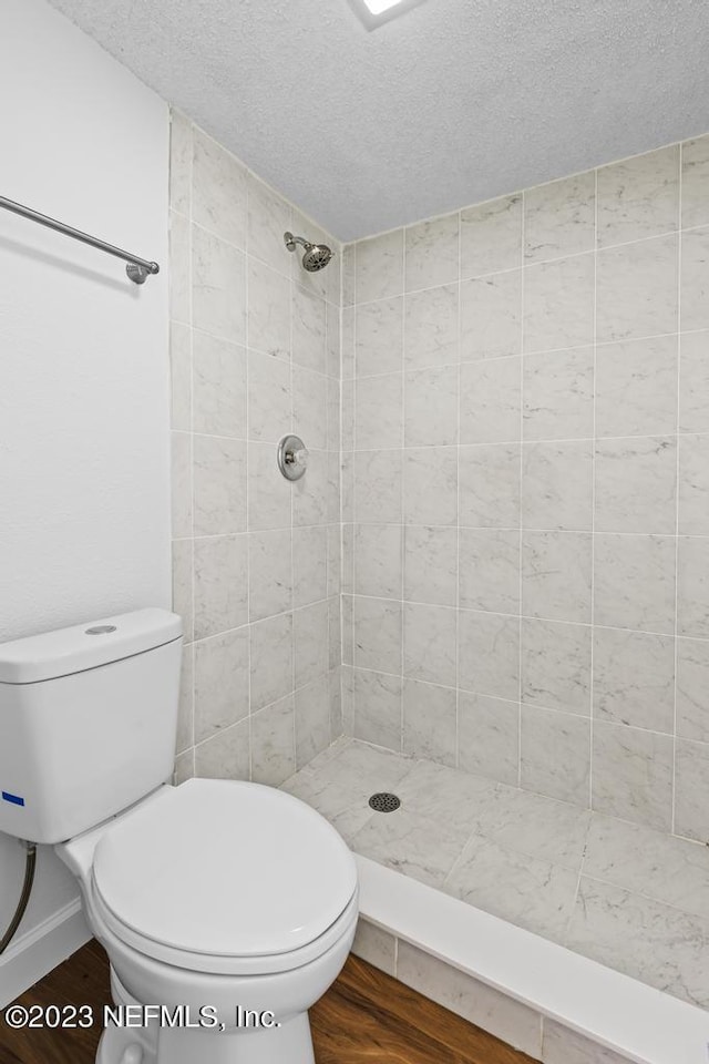 bathroom with a tile shower, a textured ceiling, toilet, and wood-type flooring