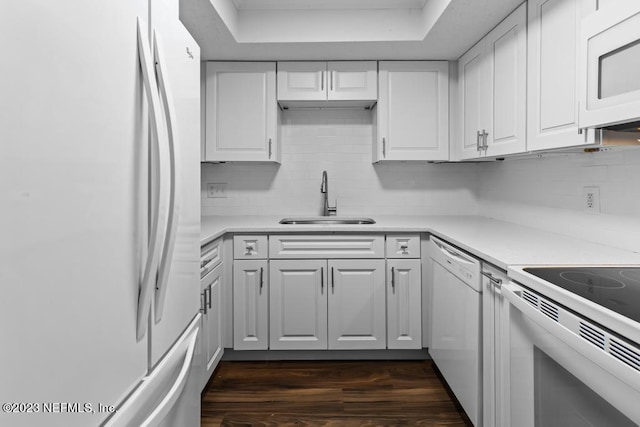 kitchen with white cabinets, a raised ceiling, sink, white appliances, and dark hardwood / wood-style floors