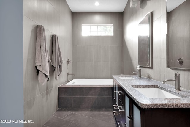 bathroom with tile patterned flooring, vanity, a relaxing tiled tub, and tile walls