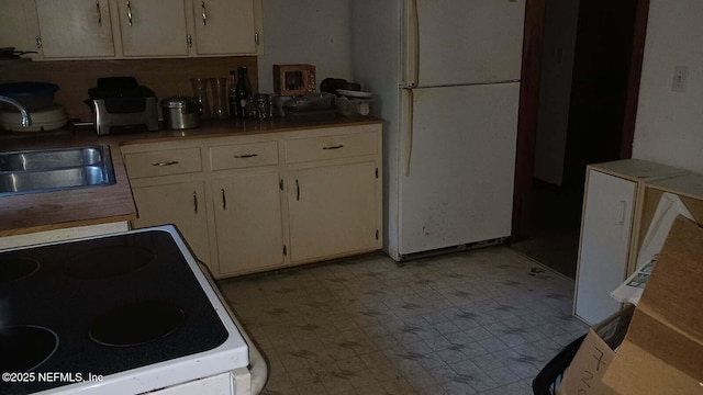 kitchen with sink, range with electric stovetop, white refrigerator, and cream cabinetry